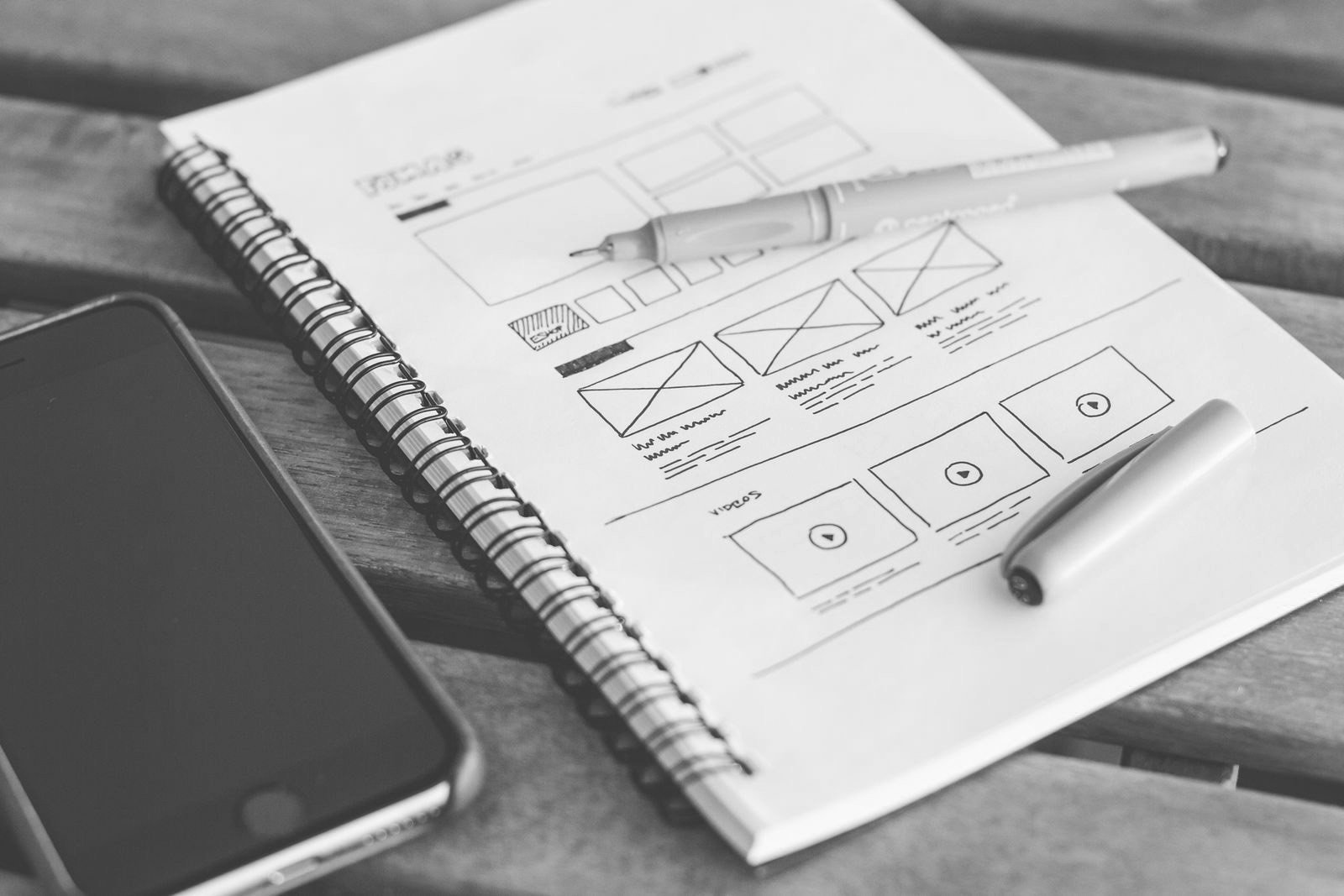 Website wireframes sketched in a notebook beside a phone